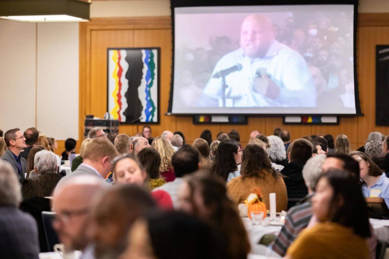 A video being played on a screen of an angry man at a board of education meeting